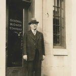 a man in a suit and hat stands in front of the general blower company