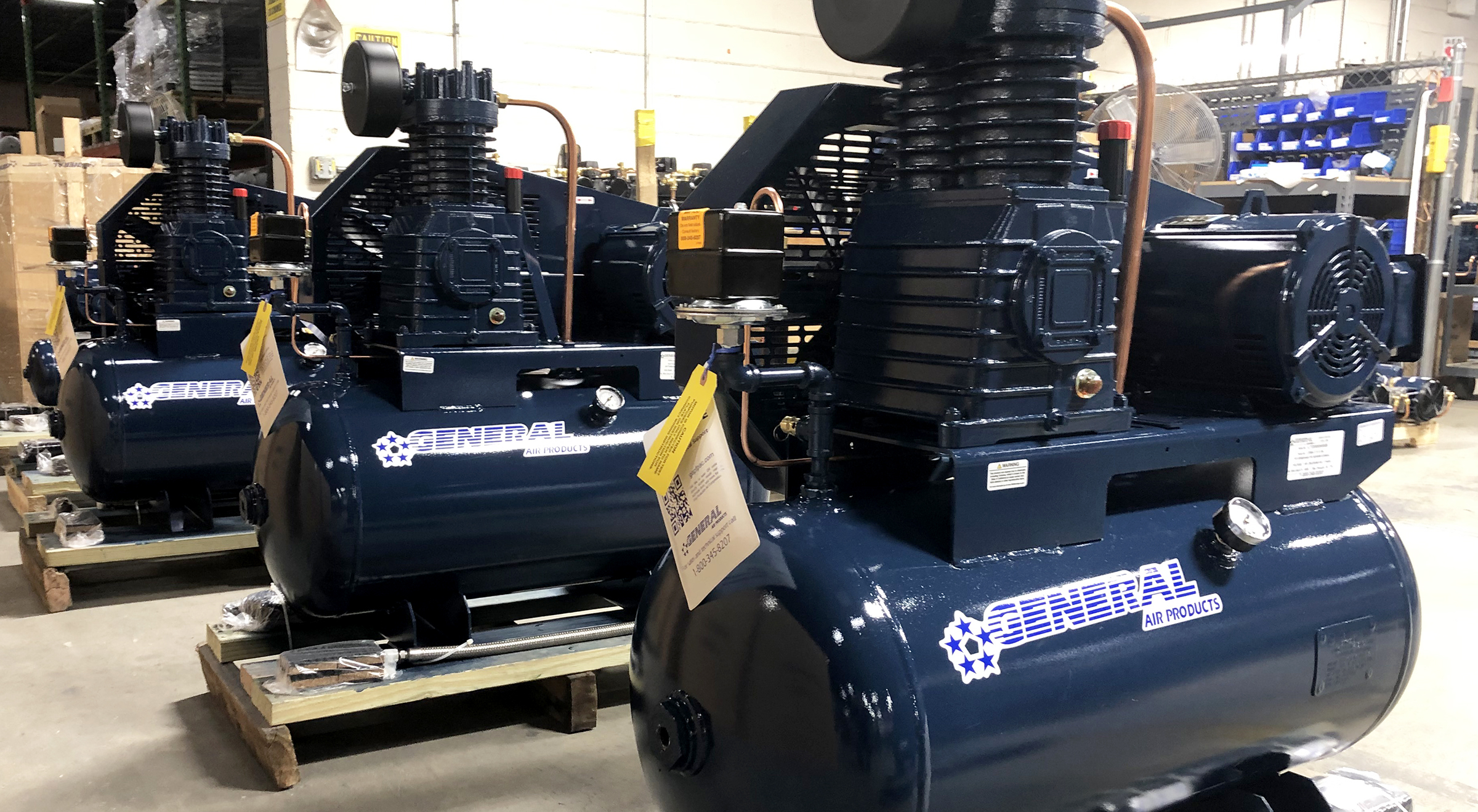 several blue general air compressors are lined up in a warehouse