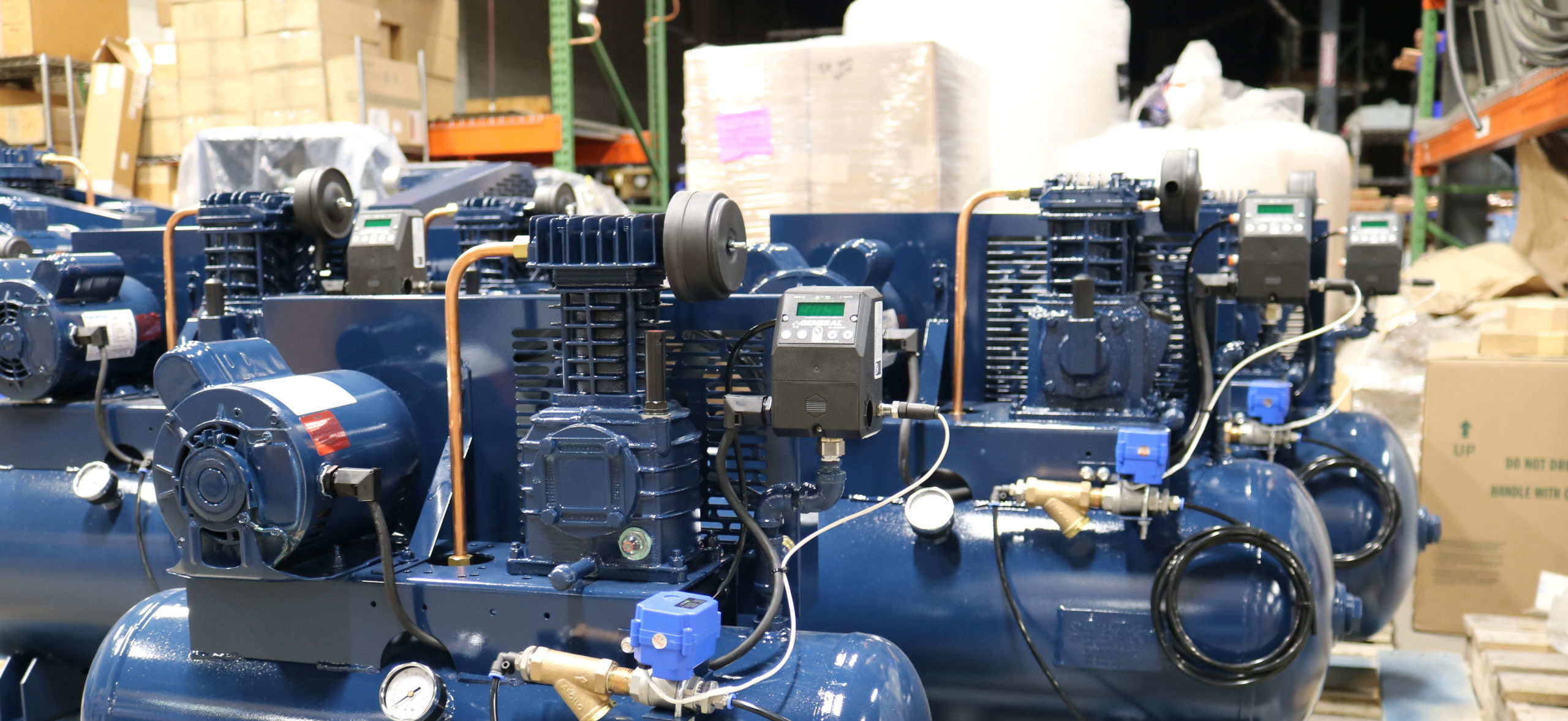 several blue air compressors are lined up in a warehouse